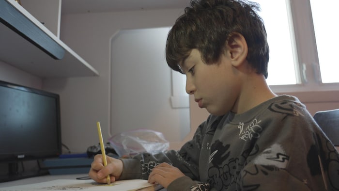 Mohammed 9 ans dessine dans sa chambre.