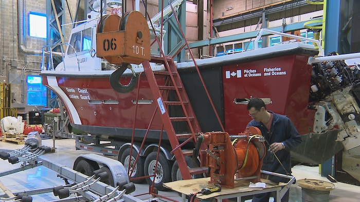 A work technician in front of a boat in a warehouse. maurice-lamontagne institute opens its doors