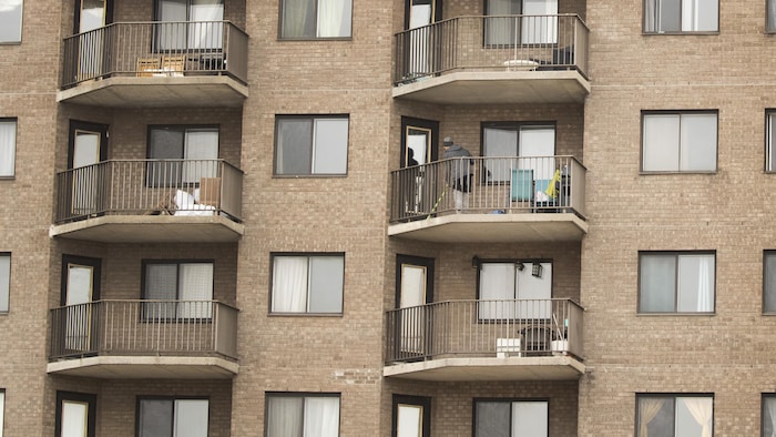 Un homme fait le ménage sur son balcon dans une grande tour d'habitation à Montréal.