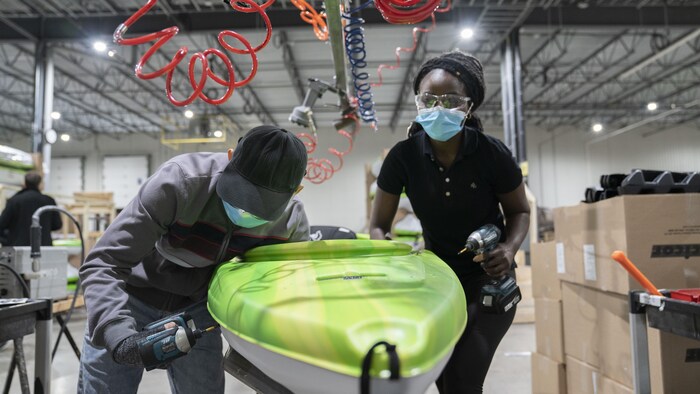 Deux travailleurs assemblent un kayak.