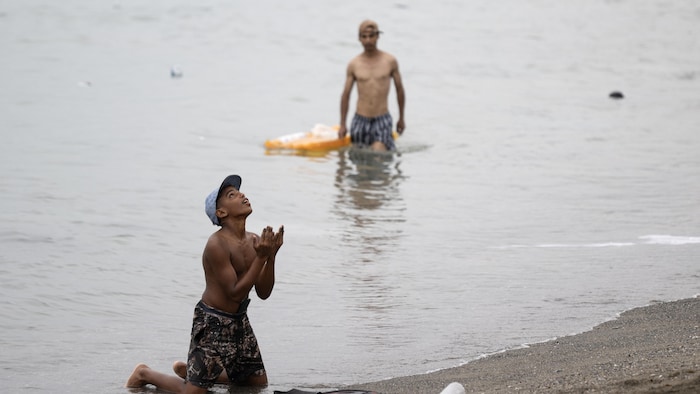 Un migrant agenouillé dans l'eau regarde vers le ciel.