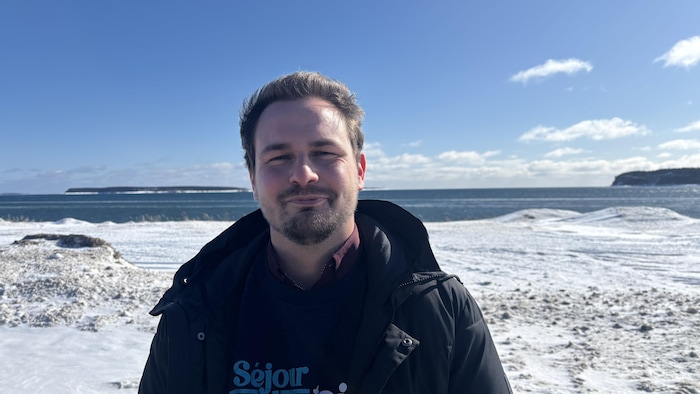 Émile Boutin avec son manteau devant le fleuve Saint-Laurent.