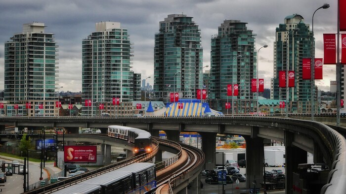 Cinq tours d'habitation et les rails du SkyTrain passant au-dessus d'un parc de stationnement à Vancouver.