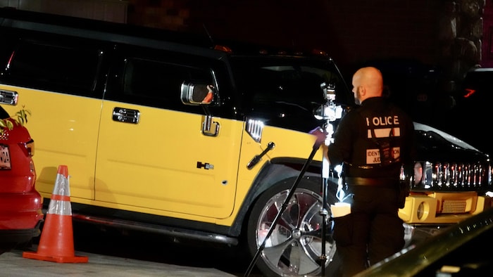 Un membre de la Section de l'identification judiciaire du SPVM photographie un trou fait par une balle dans la porte d'un gros véhicule Hummer.