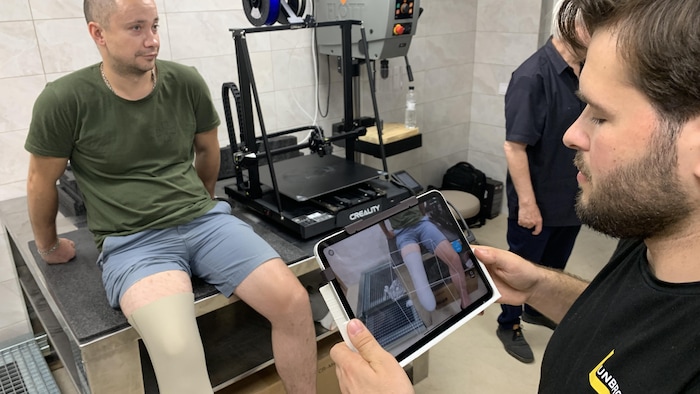 Un homme prend une photo d'un patient assis près d'une imprimante 3D.
