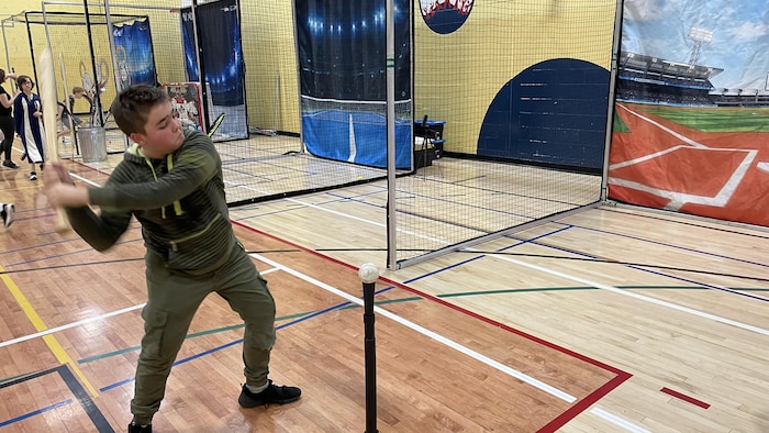 Un élève s'élance avec un bâton de baseball pour frapper une balle sur une tige de T-Ball.