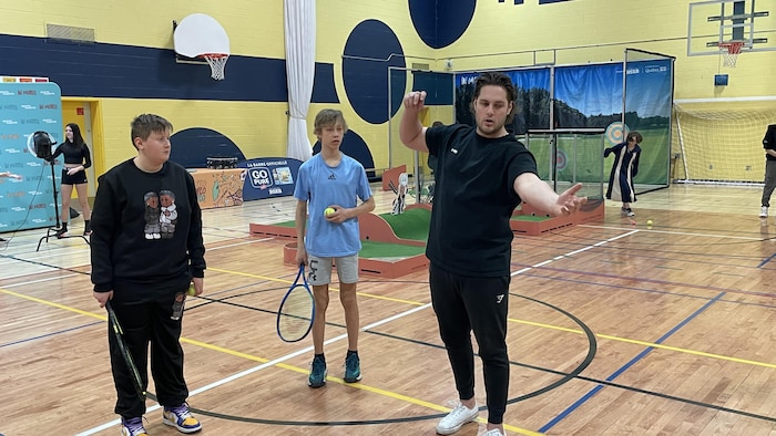 Samuel Plante enseigne à deux élèves comment servir une balle au tennis dans le gymnase de l'école Natagan de Barraute.
