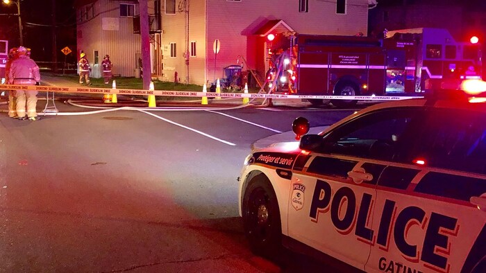 Des voitures de police et des camions de pompiers sont stationnés à proximité de l'immeuble.