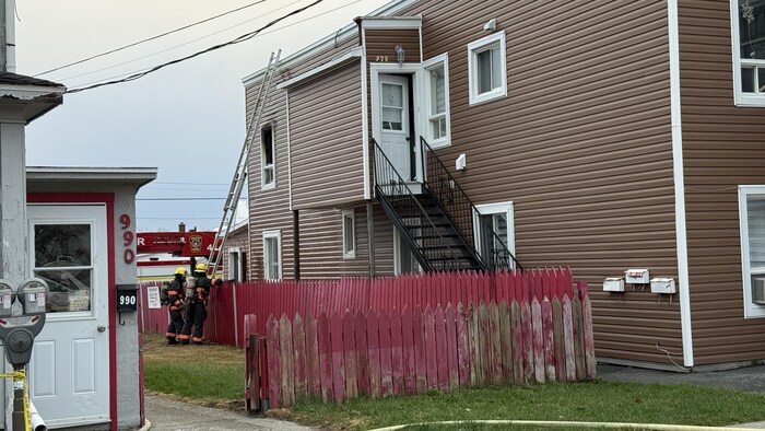 Deux pompiers au pied d'une échelle qui donne accès au toit d'un édifice.