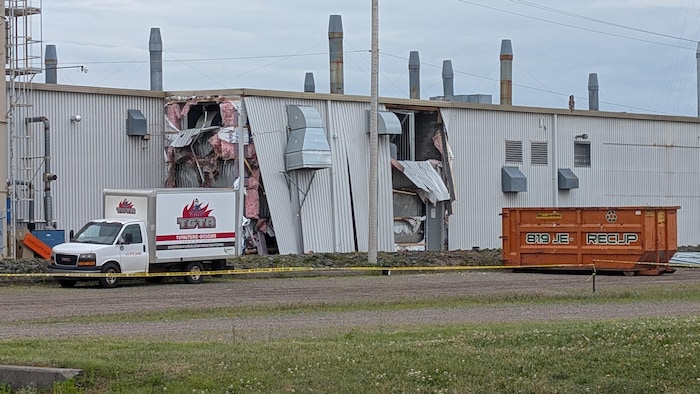 Une usine endommagée avec un conteneur à déchets et un camion à côté.