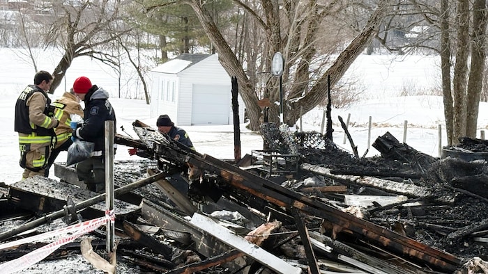 Des pompiers dans les décombres d'un chalet incendié.