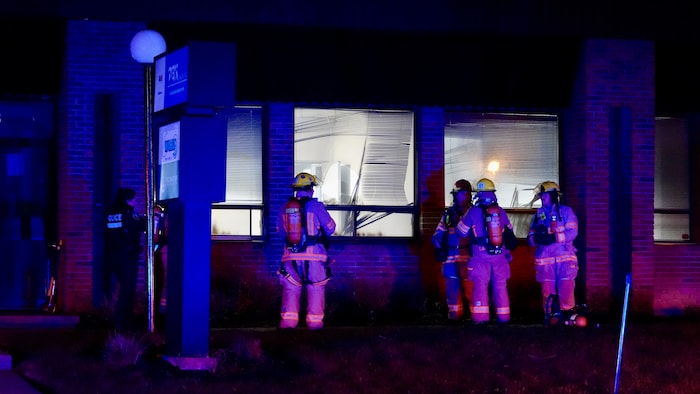 Des pompiers devant un commerce aux vitrines fracassées et incendiées.