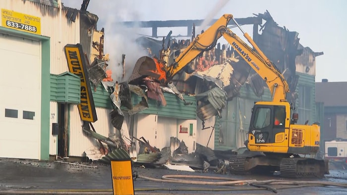 A mechanical shovel destroys the building on fire. dozens firefighters called fight fire