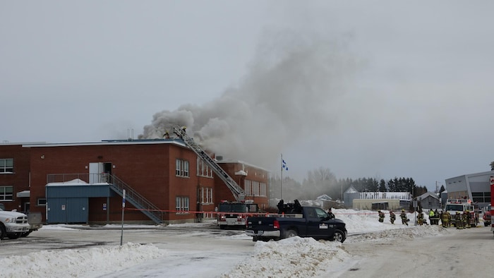 Des pompiers devant l'école d'où sort de la fumée.