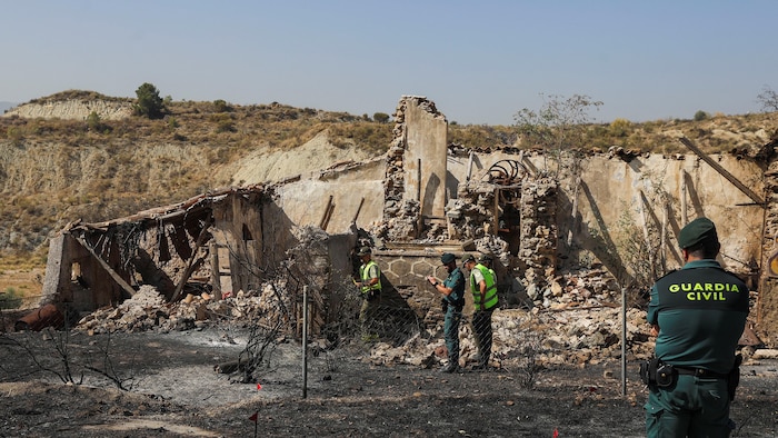 De dos, un garde civil regarde des collègues inspecter les ruines d'une maison dans un paysage brûlé