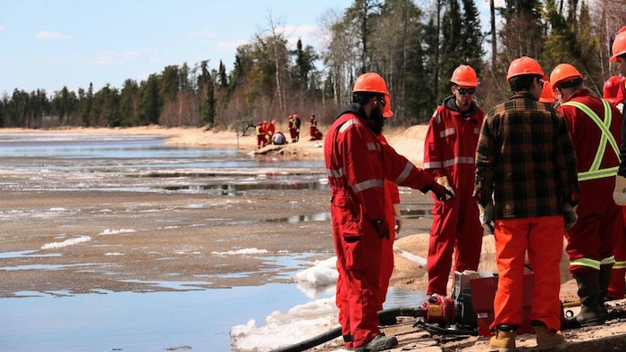 Des personnes en tenue de pompiers s'exercent devant un lac à moitié gelé.