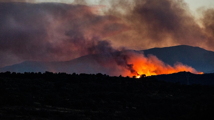 Des flammes émergent d'une montagne, à l'aube.