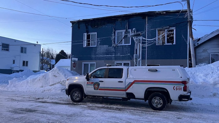 Un camion de pompier est stationné devant un bâtiment endommagé par les flammes.