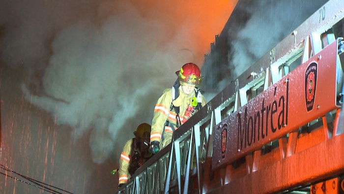 Deux pompiers de Montréal font une intervention sur les lieux d'un incendie.
