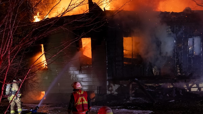 Des pompiers combattent les flammes qui consumment une maison en feu.