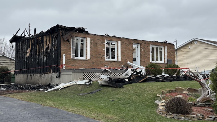 Une maison détruite par les flammes, le toit effondré, des fenêtres fracassées et des débris sur le terrain.