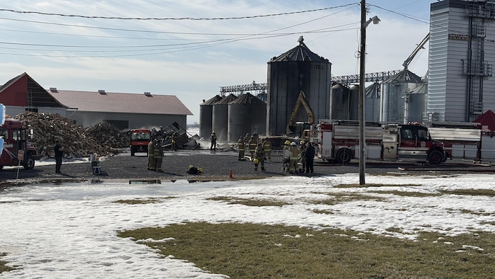 Des pompiers, des véhicules d'incendie et de la machinerie près des ruines d'un incendie.