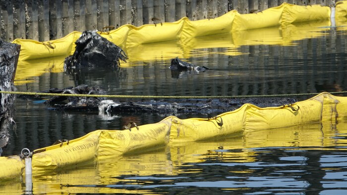 Des débris noircis par le feu, derrière une estacade flottante de plastique.