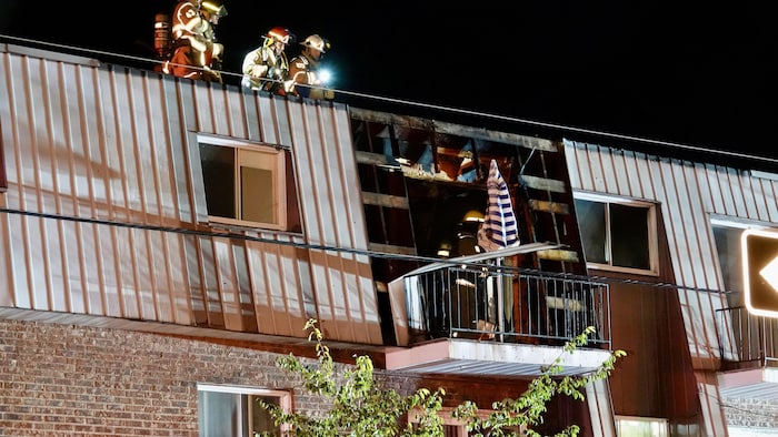 Des pompiers sur le toit et le balcon d'un bâtiment.