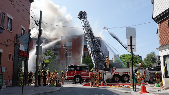 Plusieurs jets d'eau arrosent un bâtiment en flammes dans le sud-ouest de Montréal le 14 juin 2025.