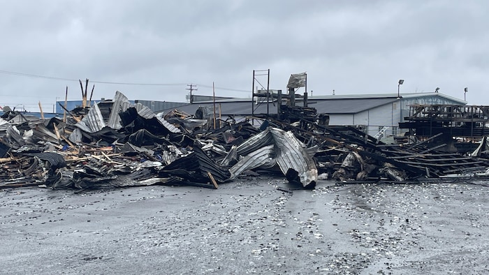 Les restes du bâtiment qui a été brûlé par l'incendie sont noircis et tordus au sol.