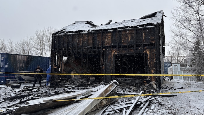 Une maison incendiée avec un policier à côté.