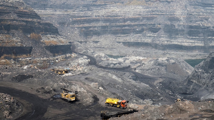 Grand trou dans la terre avec des camions de gros camions au centre, vue générale d'une mine de charbon à ciel ouvert, avec de gros camions qui transportent le matériel. 