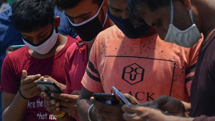 Des personnes portant des masques regardent leurs téléphones cellulaires.