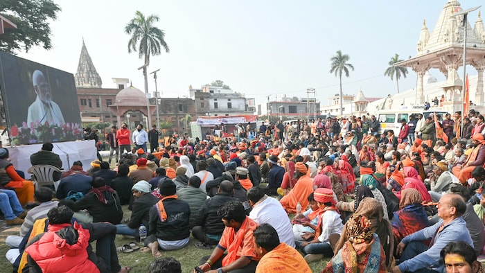 Des personnes assises dans l'herbe écoutent l'inauguration du temple Ram Mandir sur un grand écran.