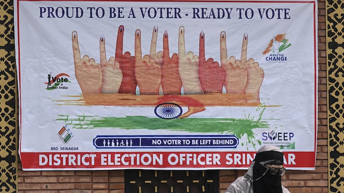 Une femme voilée devant une affiche incitant les électeurs à voter.