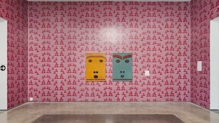 Deux tableaux d'un visage avec des yeux, des narines et une bouche en forme de rond sont accrochés à un mur.