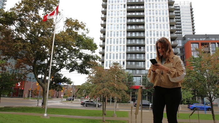 Inès Mahiou devant un immeuble qui consulte son téléphone. 