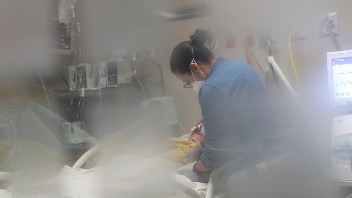 Une infirmière penchée au-dessus d'une personne couchée dans un lit d'hôpital.