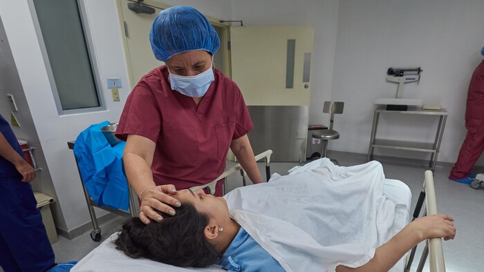 Une infirmière met la main sur le front d’une patiente couchée sur une civière.