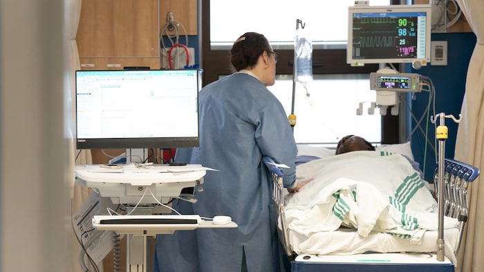 Une infirmière de dos discute avec un patient allongé dans un lit d'hôpital.






