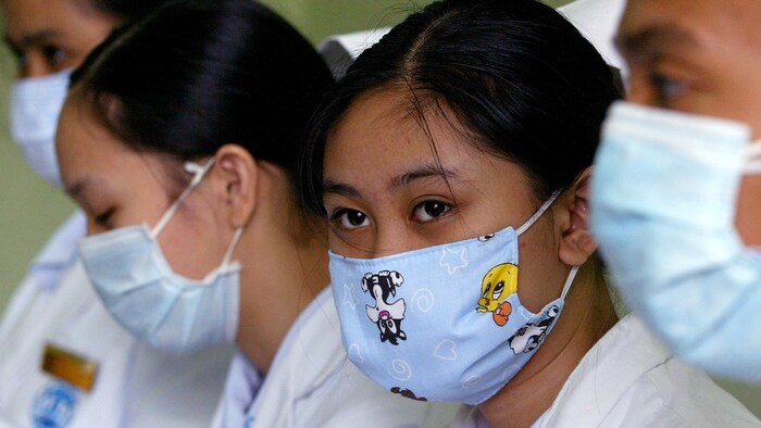 Deux étudiantes en soins infirmiers sont assises. Elles ont des uniformes blancs et des masques sur le visage. L'une d'entre elles a un masque décoré de dessins de Tweety et Sylvester.