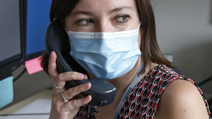 Une femme au téléphone devant un ordinateur porte un masque.
