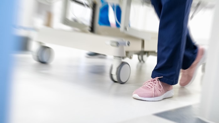 Plan rapproché des jambes d'une infirmière chaussée de souliers de course roses, à côté des roues de la civière qu'elle tire.