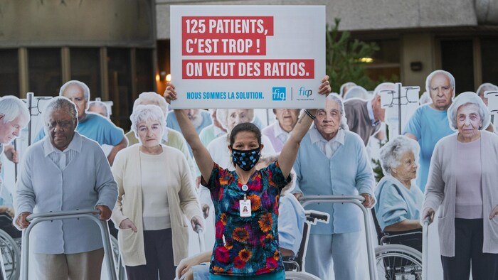 Une membre de la FIQ tenant une pancarte entourée de dizaines d'effigies représentant des patients de CHSLD.