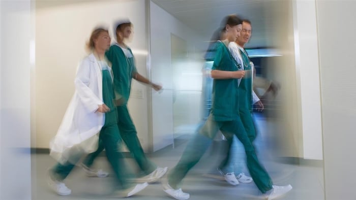 Plan large et flou de quatre travailleurs de la santé marchant dans un corridor d'hôpital.