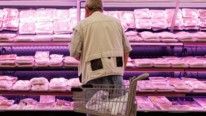 Une personne âgée devant un rayon de viande.