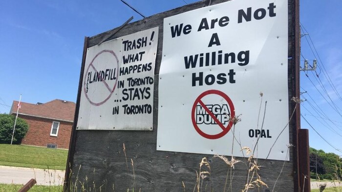 Pancartes en anglais sur lesquelles on peut lire: «Trash! What happens in Toronto stays in Toronto» et «We are not a willing host».