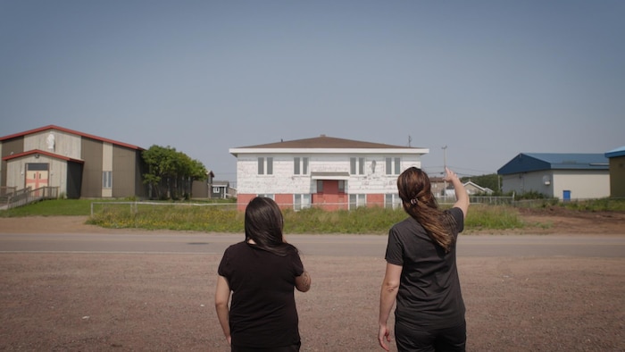 Deux personnes de dos regardent une maison au loin.