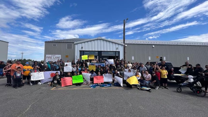 Des personnes se rassemblent devant un aréna avec des pancartes.
