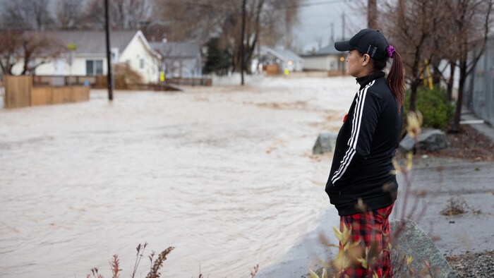 Une résidente de Merritt, en Colombie-Britannique, observe une rue inondée dans laquelle se trouve une maison partiellement submergée, le lundi 15 novembre 2021.